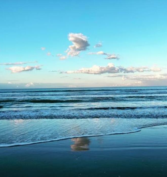 Spiaggia serena con cielo azzurro e nuvole.