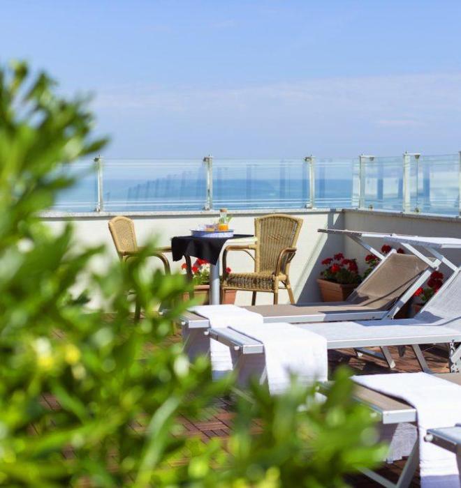 Terrazza con lettini, tavolo e vista mare, circondata da piante.