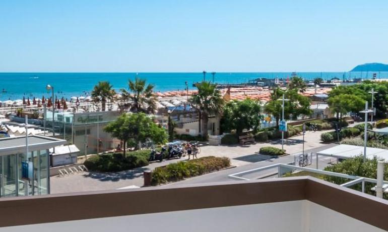 Vista sul mare con spiaggia e palme, giornata soleggiata.