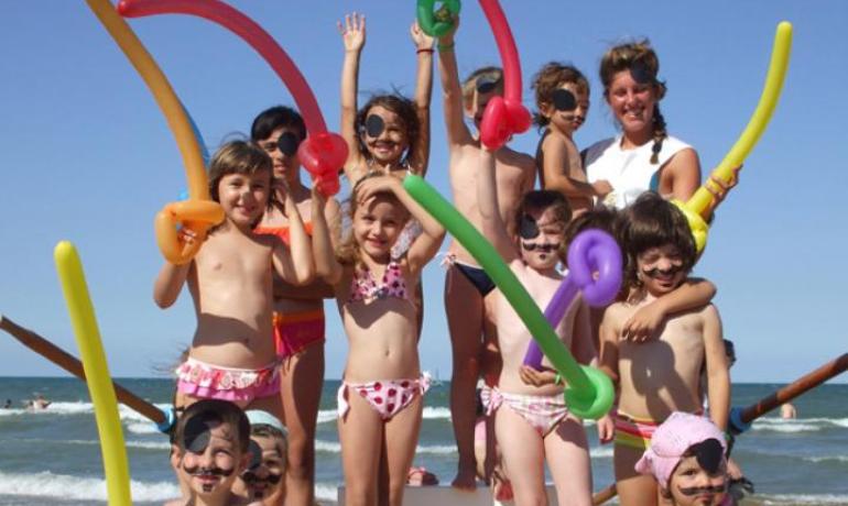 Bambini vestiti da pirati sulla spiaggia con spade gonfiabili.