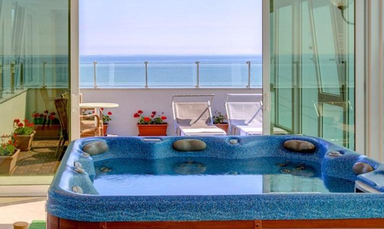 Jacuzzi con vista mare, sdraio e fiori sul balcone.