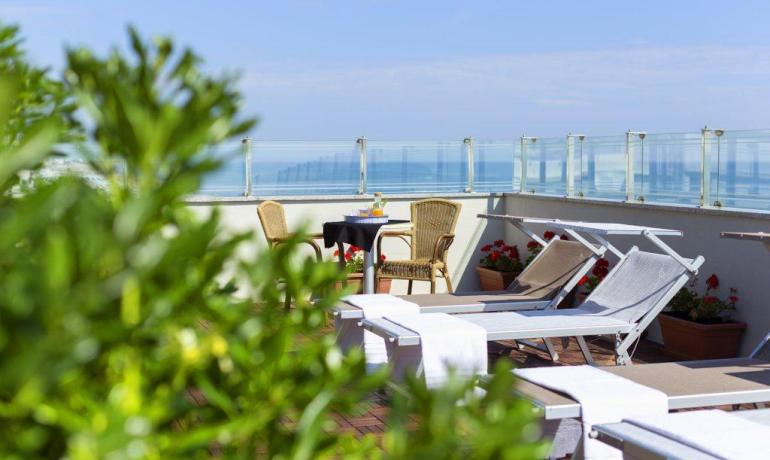 Terrazza con lettini, tavolo e vista mare, circondata da piante.