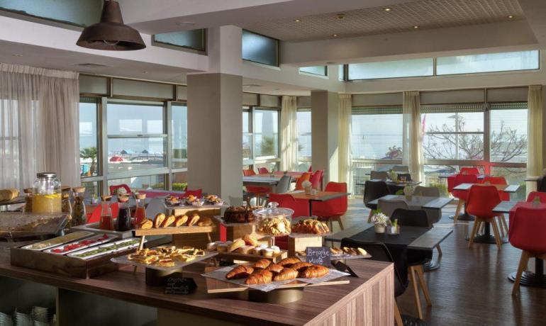 Sala colazione luminosa con buffet di dolci e vista mare.