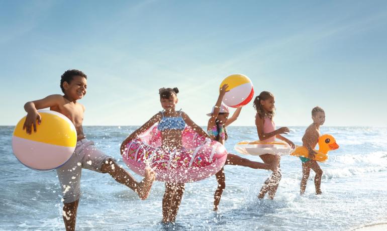 Bambini giocano felici in mare con gonfiabili e palloni.